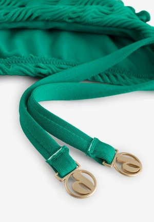 Curea din țesătură culoarea teal, cu capete cu textură nervurată, prevăzute cu catarame rotunde din metal auriu cu design decupat, așezată pe un material țesut asortat.