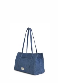 Sac cabas en denim bleu avec double bretelles et une petite étiquette rectangulaire sur la poche avant, sur un fond blanc.