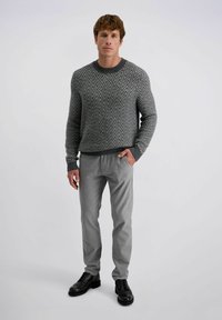 Grau gemusterter Pullover mit Zickzackmuster und geripptem Halsausschnitt, kombiniert mit hellgrauen Hosen und schwarzen Schnürschuhen. Schlichtes, strukturiertes Design.