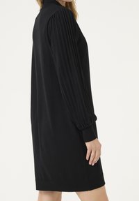 Robe noire avec manches bouffantes côtelées, coupe droite et encolure arrondie. Tissu en maille à texture lisse avec une finition d'ourlet.