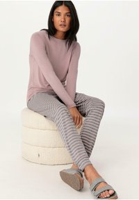 Soft pink long-sleeve top, gray striped leggings with a smooth texture, and gray slippers with a cork sole, seated on a round, fuzzy pouf.