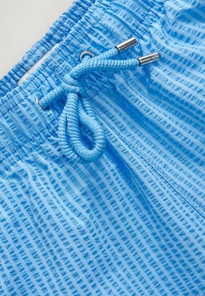 Light blue swim shorts featuring a textured fabric with vertical stripes, an elasticated waistband, and a matching drawstring with metal tips.