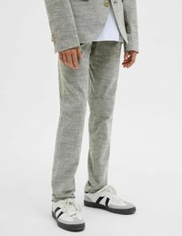 Grå, texturerade kostymbyxor i kombination med vita och svarta sneakers. Klädseln har en skräddarsydd passform och en subtil lyster i tyget.