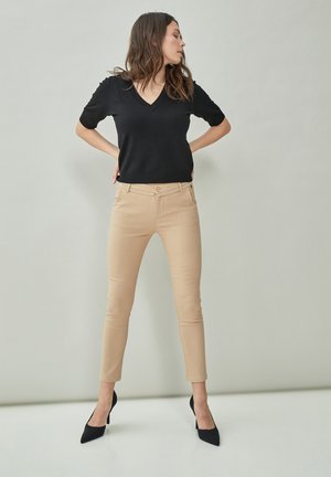 Black short-sleeve V-neck top paired with beige fitted pants and black pointed-toe heels. Smooth fabric with minimal detailing.
