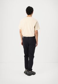Heren beige t-shirt met een ronde hals, gecombineerd met donker marineblauwe broek, voorzien van een subtiele gele accenten op de achterzak en een gestructureerde stof.