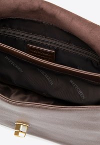 Interieur van een bruine leren tas met een gladde textuur, voorzien van een ritsvak en een gemerkte stoffen voering met herhalende patronen. Accenten in goudkleurig metaal.