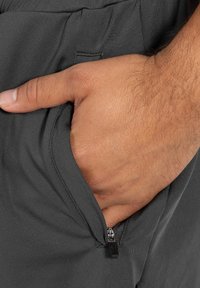Graue Hose mit glatter Textur und einer Reißverschlusstasche. Die Tasche verfügt über einen eleganten schwarzen Reißverschluss und ist auf Praktikabilität ausgelegt.