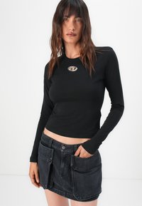 Black long-sleeve fitted top with a logo on the chest, paired with a dark denim skirt featuring large front pockets and a button closure.