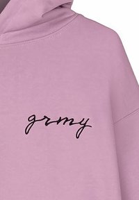 Sudadera con capucha de tela rosa claro que presenta un logo bordado en negro "grmy" en el lado izquierdo. Textura suave y diseño de corte relajado.