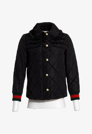 Schwarze gesteppte Jacke mit Rüschenkragen, goldenen Knöpfen vorne und grün-rot gestreiften gerippten Bündchen an den langen Ärmeln.