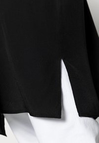 Maglietta nera con uno spacco laterale e orlo nero, stratificata su tessuto bianco. Texture liscia, con un design elegante e minimalista.