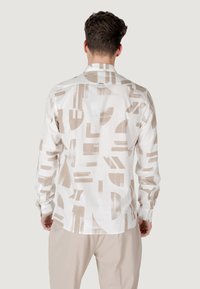 Camisa blanca con patrones abstractos en beige, con un cuello clásico y mangas largas, fabricada en tejido ligero.