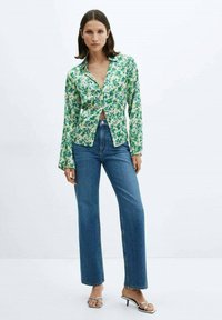 Bloemige button-up shirt in groene en blauwe tinten, gemaakt van gladde stof. Gecombineerd met hoge blauwe jeans en zilveren hakken.
