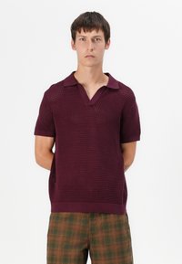 Polo en tricot bordeaux avec un col en V et des manches courtes, arborant un motif texturé et un col uni contrastant.