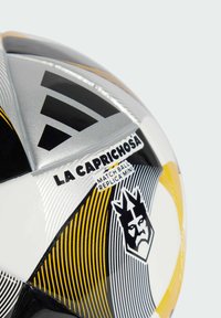 Crno-bijela i žuta nogometna lopta s geometrijskim uzorcima, koja sadrži natpis "LA CAPRICHOSA" i logo krune; sjajna površina, teksturirani dizajn.
