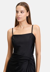 Schwarzes Satin-Kleid mit quadratischem Ausschnitt, dünnen Trägern und verdrehtem Detail an der Taille, das eine glatte Textur und eine figurbetonte Passform bietet.