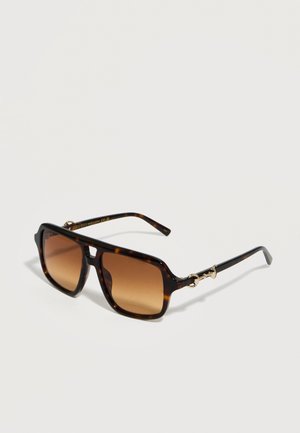 Lunettes de soleil rectangulaires en écaille de tortue avec des verres dégradés marron et des détails dorés sur les branches, sur un fond uni.