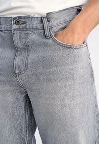 Jasnoszare dżinsy z denimu o swobodnym kroju, z przednią kieszenią, metalowym guzikiem i subtelną fakturą tkaniny.