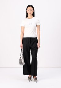 T-shirt blanc avec un design de papillon, associé à un pantalon noir à jambes larges. Les accessoires incluent un sac à main argenté métallique et des chaussures argentées.