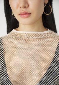  Gjennomsiktig mesh topp i en nøytral farge, med et diamantmønster, myk halslinning og åpen veving, kombinert med en svart stoffbase. Gule hoop-øreringer.