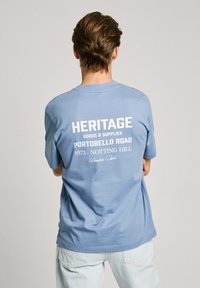 Light blue cotton T-shirt with short sleeves, featuring a white printed design on the back that includes text and accents.