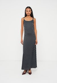 Robe longue noire à pois blancs, dotée de bretelles spaghetti, d'une coupe décontractée et d'une silhouette droite. Texture de tissu lisse.