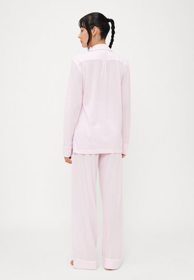 Ροζ πυτζάμα που περιλαμβάνει μπλούζα με μακριά μανίκια και γιακά καθώς και παντελόνι με φαρδύ μπούστο. Το ύφασμα φαίνεται λείο με ελαφρώς γυαλιστερή υφή.