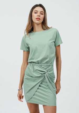 Abito verde menta con corpino attillato e vita elastica, caratterizzato da un dettaglio annodato sulla gonna. Realizzato in tessuto morbido ed elastico.