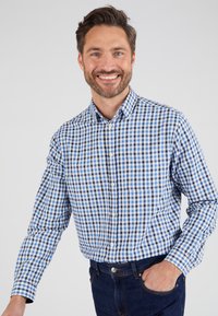 Camicia a quadri blu e bianca con maniche lunghe, colletto e tasca sul petto; abbinata a jeans in denim scuro.