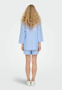 Lichtblauw gestreept shirt met korte mouwen en bijpassende shorts, gemaakt van een zachte stof, met een losse pasvorm en een gebogen zoom. Witte schoenen zichtbaar.