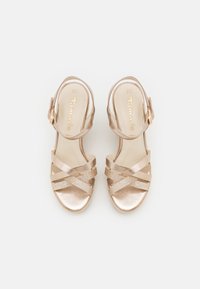 Sandały na ramiączkach w metalicznym złocie i jasnym beżu, z mieszanką gładkich i błyszczących ramiączek, z zapięciem na kostce oraz płaską podeszwą.