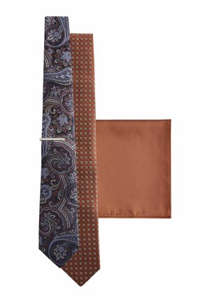 Zwei Krawatten, eine mit blauem Paisley-Muster und die andere braun mit kleinen geometrischen Formen, neben einem passenden braunen Einstecktuch gelegt.