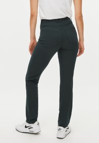 Pantaloni verde scuro realizzati in tessuto elasticizzato, con un design aderente, due tasche posteriori, indossati con sneakers bianche Nike.