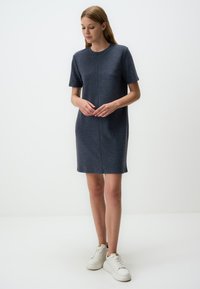 Kurzes, grauschwarzes Kleid aus weichem Material, mit Rundhalsausschnitt und geradem Schnitt, kombiniert mit weißen Sneakers.