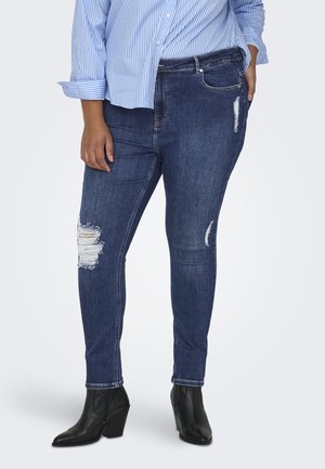Dark blue denim skinny jeans with distressed knee details. Features a standard five-pocket design and contrast stitching, paired with black ankle boots.