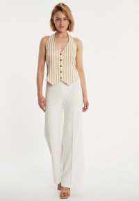 Gestreifter Halter-Vest in Creme und Beige mit V-Ausschnitt und Knopfdetails, kombiniert mit hochgeschnittenen weißen weit geschnittenen Hosen.