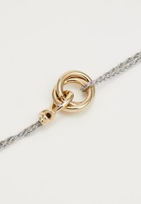Collana a catena d'argento intrecciata con chiusura circolare in oro lucido su uno sfondo bianco semplice.