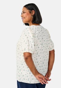 Floral print blouse in cream, with puff sleeves and a straight cut. Features small blue and green flowers against a textured fabric.