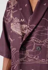 Lila Kurzarmhemd mit detailliertem Kartenmuster in hellem Rosa, mit aufgeschlagenem Revers und doppelter Knopfschließe. Glatte Stoffbeschaffenheit.