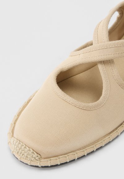 Μπεζ εσπαντρίγια με σχεδιασμό με σταυρωτό λουρί, επάνω μέρος από καμβά, υφή επιφάνειας και πλεκτή γιούτα κατά μήκος της άκρης. Εμφανίζεται ανοιχτό μπροστινό μέρος.