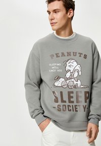 Szara bluza z miękkiego materiału, z graficznym nadrukiem Snoopy'ego śpiącego z napisem "PEANUTS SLEEP-SOCIETY" w kolorze brązowym.