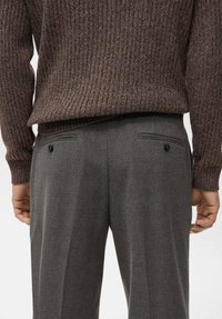 Pantalones de lana gris con una textura suave y bolsillos traseros, combinados con un suéter marrón de canalé. Los pantalones tienen detalles sutiles de costura.