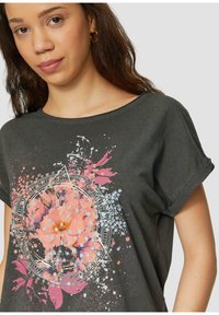T-shirt gris foncé à col rond et manches courtes, présentant un graphique floral dans des tons roses et bleus, avec des éclaboussures de peinture dispersées.