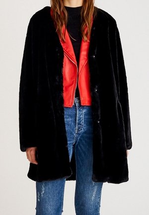 Frau trägt einen schwarzen Kunstpelzmantel über einer roten Lederjacke, kombiniert mit blauen, ausgewaschenen Skinny-Jeans.