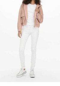 Rosa, kort, zip-up jacka med texturerad yta och elastiska ärmar, ihop med en vit tajt t-shirt och vita skinny jeans. Vita sneakers.