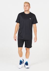 Svart atletisk t-shirt med korta ärmar och rundad halsringning, kombinerad med svarta shorts. Påfallande vitt logotypsaccent på bröstet.