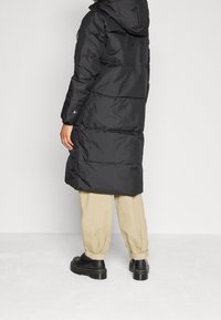 Černá zateplená parka s kapucí, s dlouhým střihem, prošívanou strukturou a cvočky na manžetách.