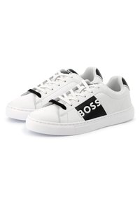 Hvite lær sneakers med svart logo og detaljer, som har en teksturert gummisåle, rund tå og tradisjonelle snøringer.