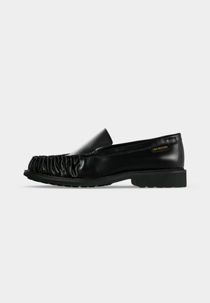 Fekete bőr loafers, elején ráncolt résszel és alacsony, masszív talppal, oldalán kis "Love Moschino" márkajelzéssel.