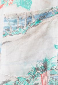 Camisa de manga corta confeccionada con una tela ligera que presenta un estampado de hojas de palma y un paisaje en tonos verdes, azules y coral. Incluye un pequeño bolsillo en el pecho.